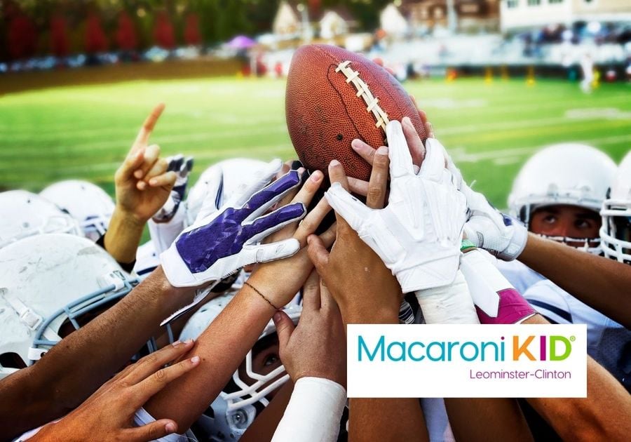 Hands of football team players holding up a football on the field.