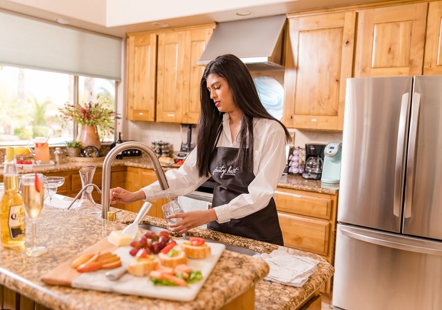 woman with apron getting water from kitchen faucet