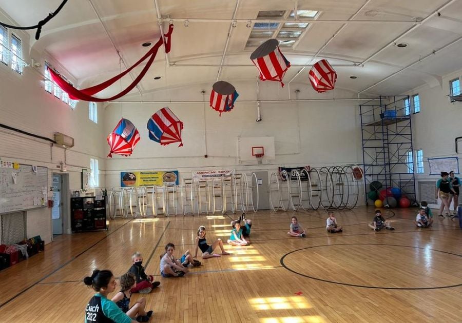 kids sitting on gym floor with american flag lanterns in the ceiling