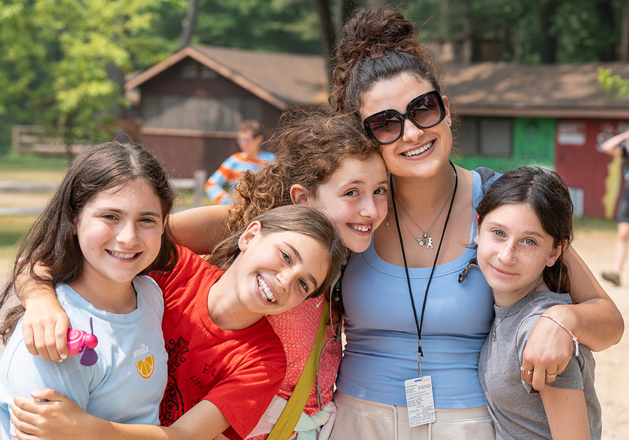 4 girls with their camp counselor in front of cabin