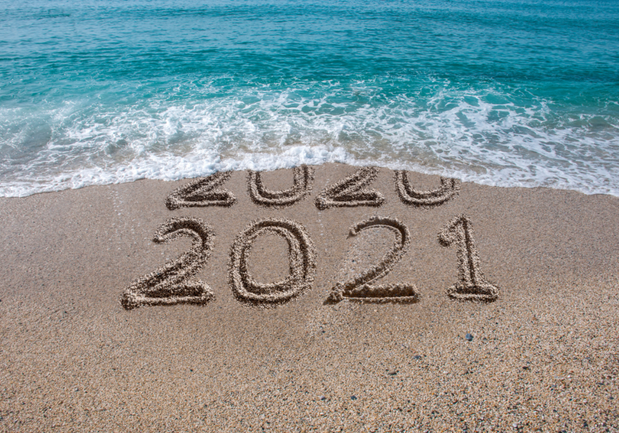 2020 and 2021 written in the sand with a wave washing 2020 away