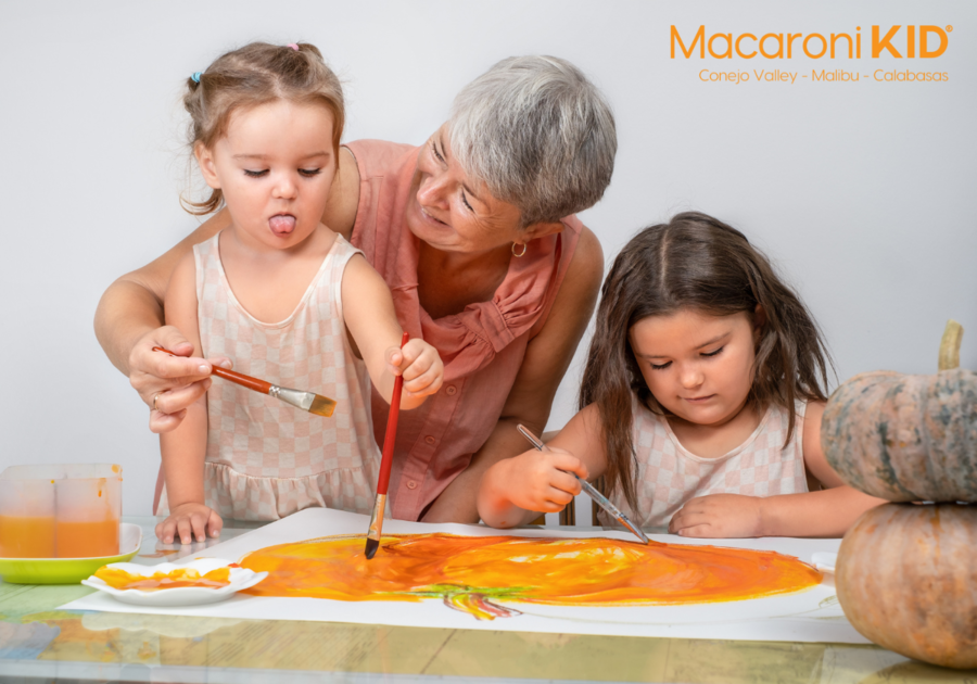 2 girls painting a big pumpkin on paper  with grandma