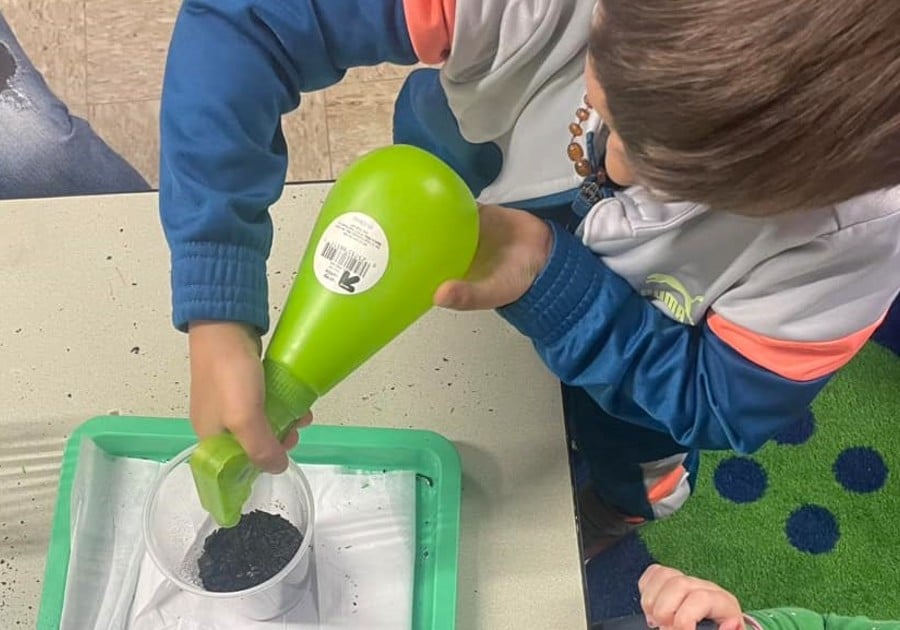 photo of male student spraying water on soil in cup