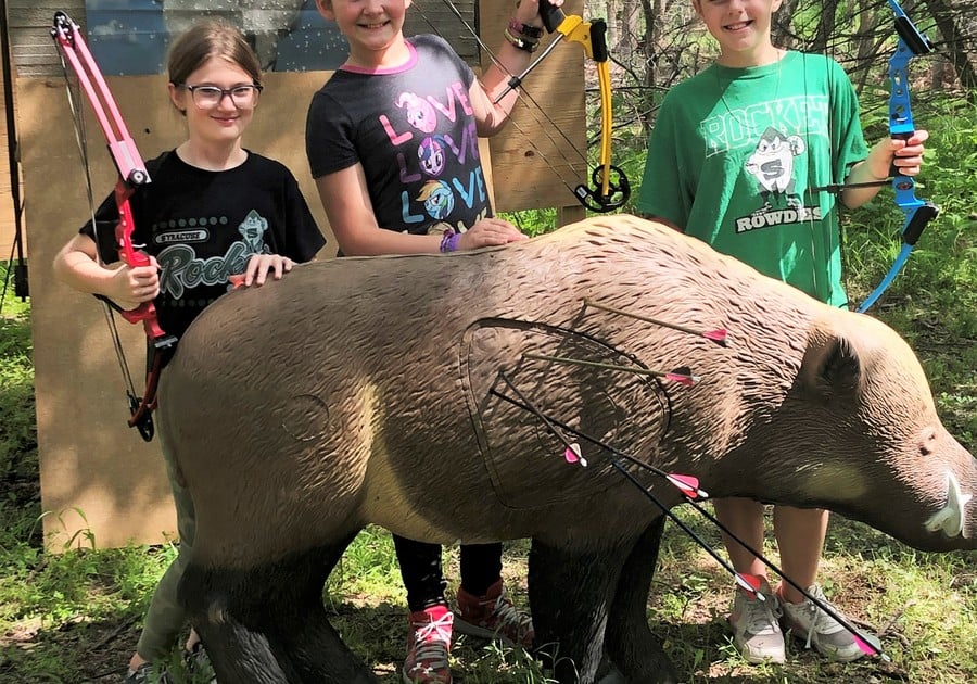 Three girls holding bows by fake boar.