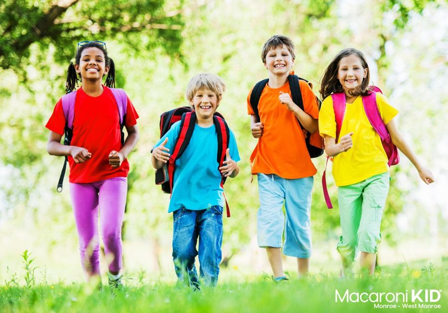 Four kids running down a dirt road in bright colored clothes with backpacks on.